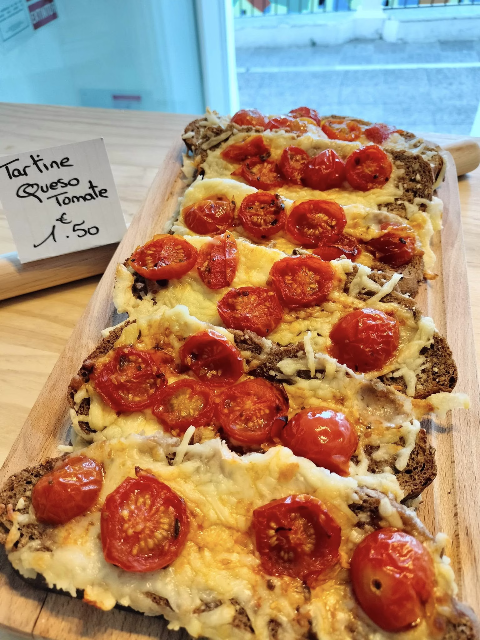 Rebanada de pan rústico con queso fundido y tomate fresco. / Rustic bread slice topped with melted cheese and fresh tomato.
