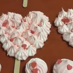Merengues en forma de corazón sobre papel de horno, listos para hornear en el obrador de El Epicúreo.