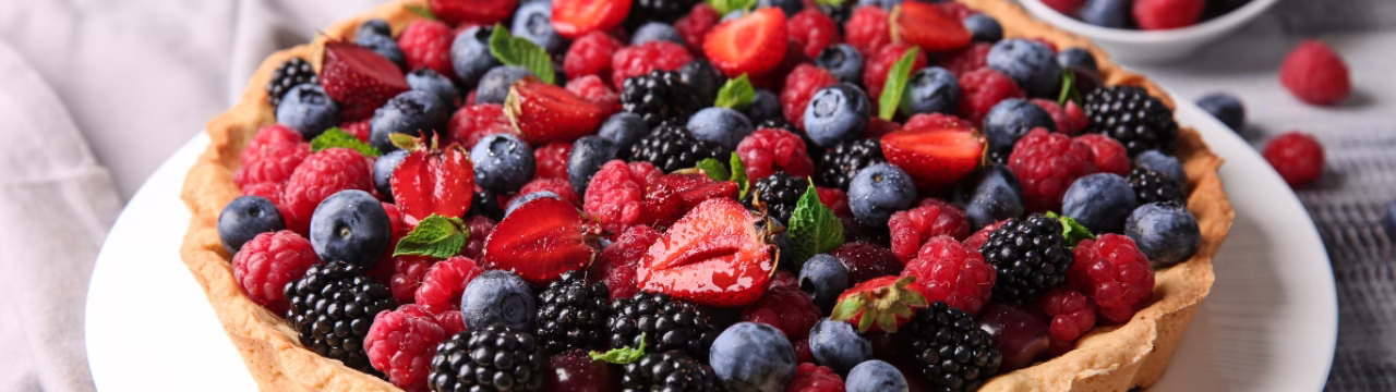 Primer plano de una tarta de frutos rojos frescos con base de masa quebrada y crema de vainilla.