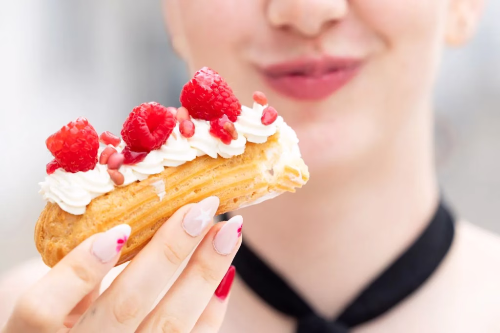Primer plano de un éclair decorado con nata y frambuesas frescas, fotografiado por Matthias Winter.