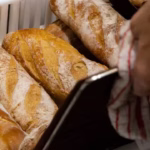 Manos de un panadero sacando barras de pan recién horneadas de una bandeja en El Epicúreo.