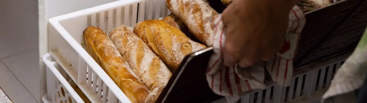 Manos de un panadero sacando barras de pan recién horneadas de una bandeja en El Epicúreo.