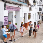 Familias y niños con mochilas reunidos frente a la fachada de la panadería El Epicúreo en Cómpeta durante la vuelta al cole.